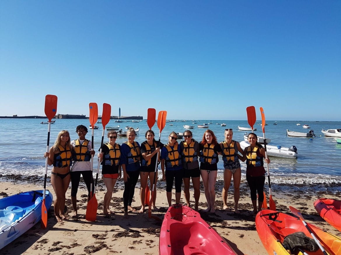 Students on beach with kayak paddles and kayaks
