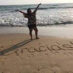 Ruth standing on beach with word 'gracias' written in the sand