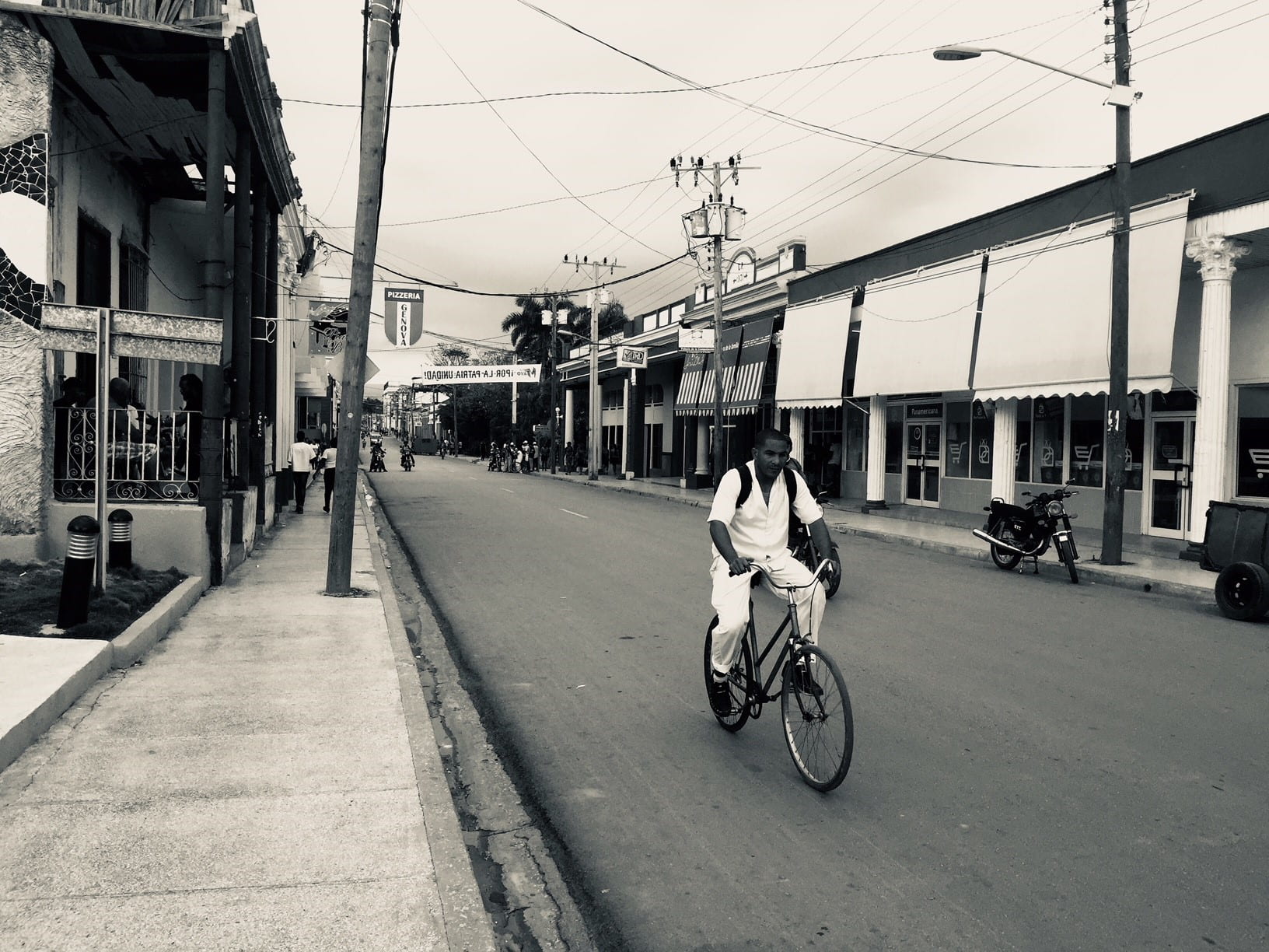 Black and white photo of person riding bicycle in middle of street in Havana, Cuba
