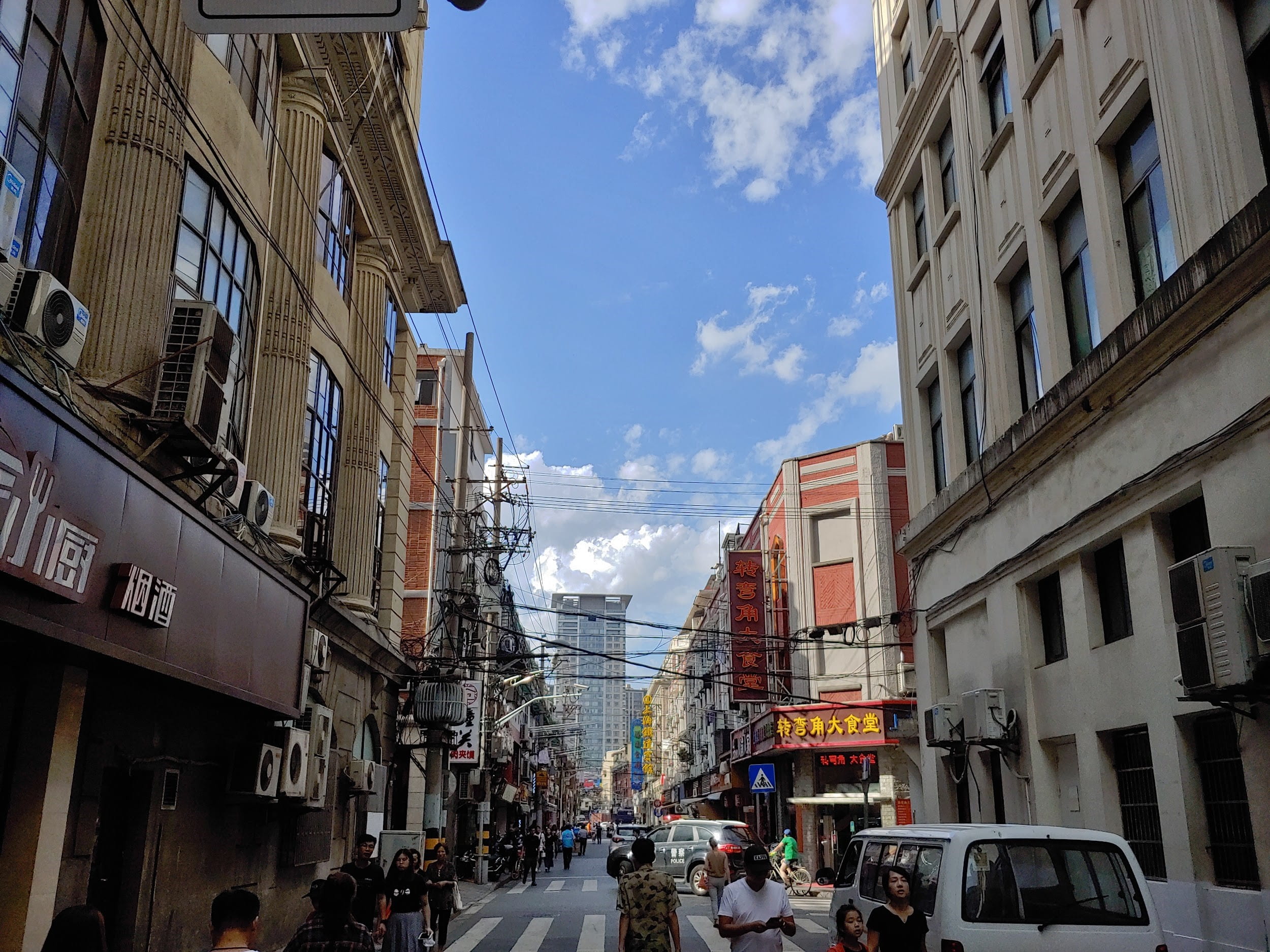 Looking down a street in Shanghai with buildings on both sides and blue sky and clouds in the background