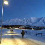 Student walking on dimly-lit path in snow with snowy mountains in background