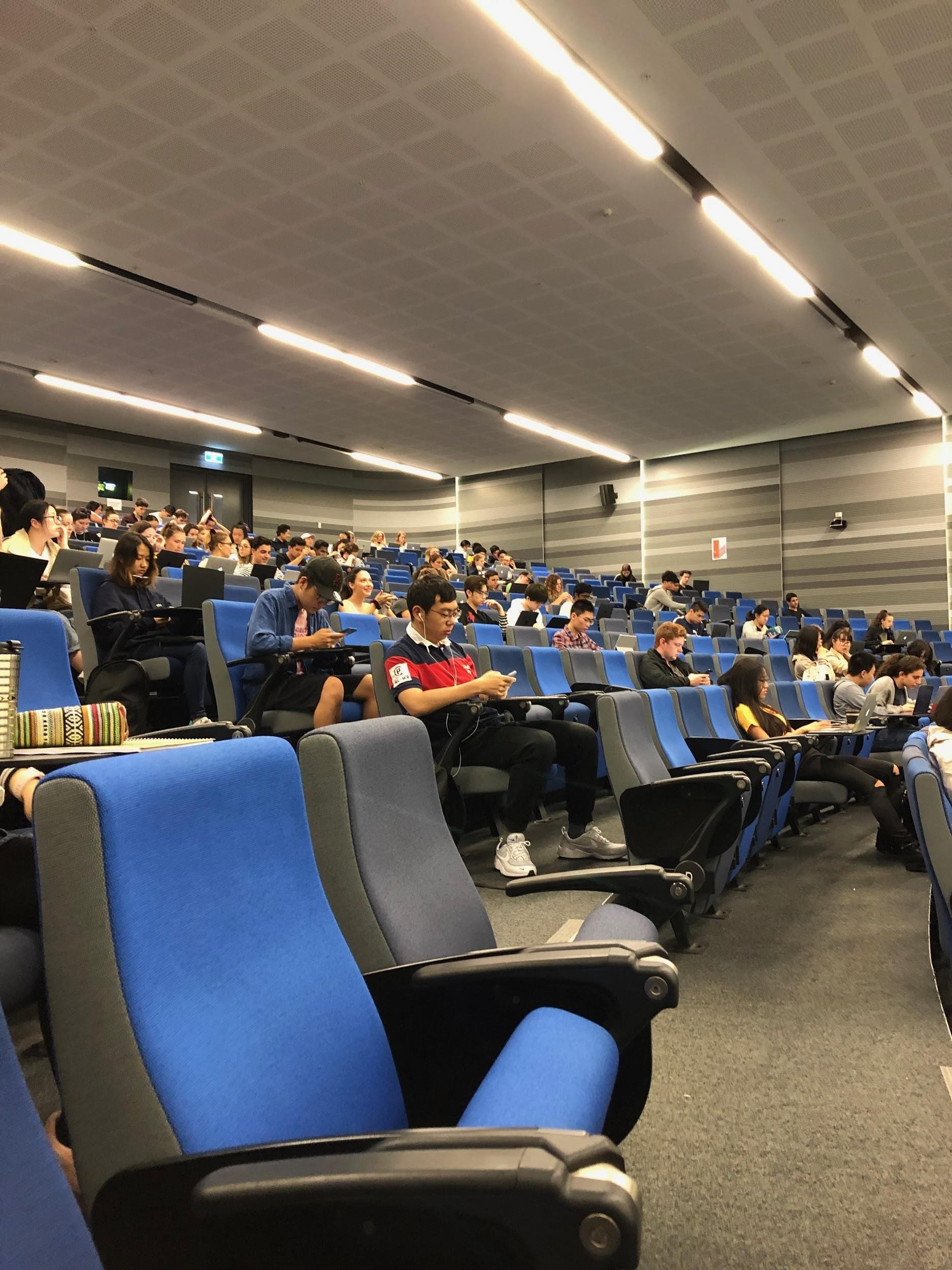 large lecture hall with blue seats and half full of students