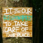 Wood sign with words painted in white and green reading, "It is our responsibility to take care of this place."