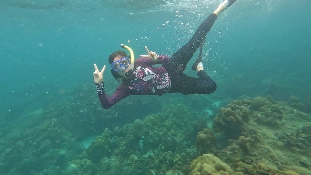 Anna is snorkeling underwater giving two "peace" signs