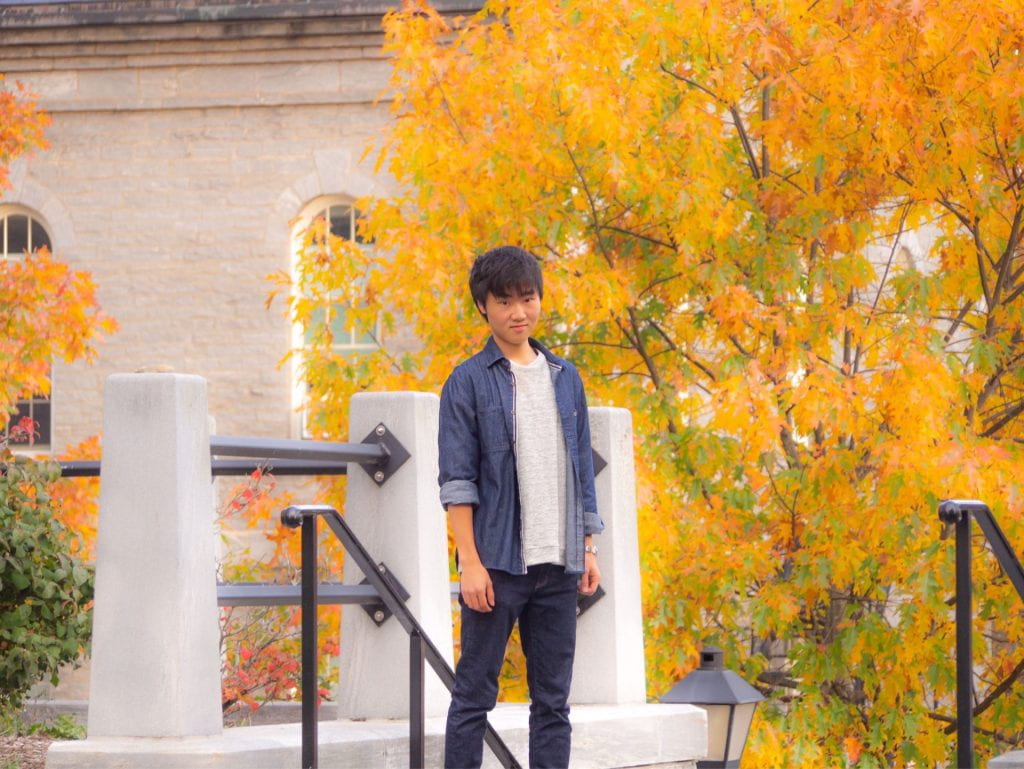 Harufumi poses on a set of stairs in front of a tree with bright yellow leaves