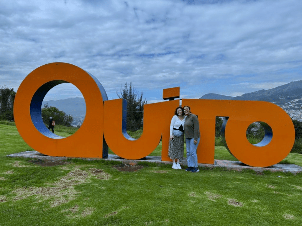 Maddie and a friend standing in front of the sign showing the capitol of Ecuador, Quito.