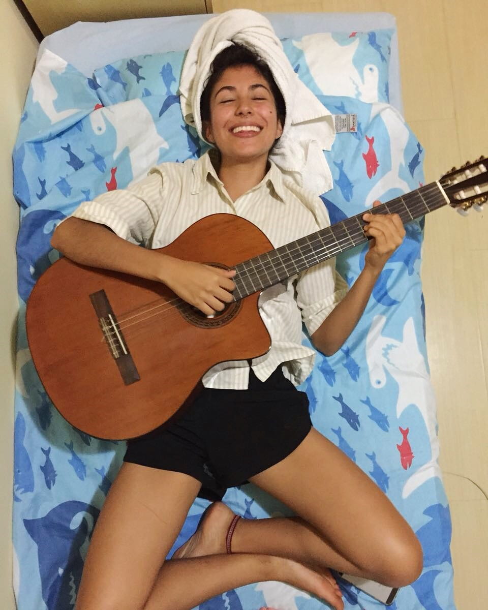 Esperanza lying on a bed, playing guitar