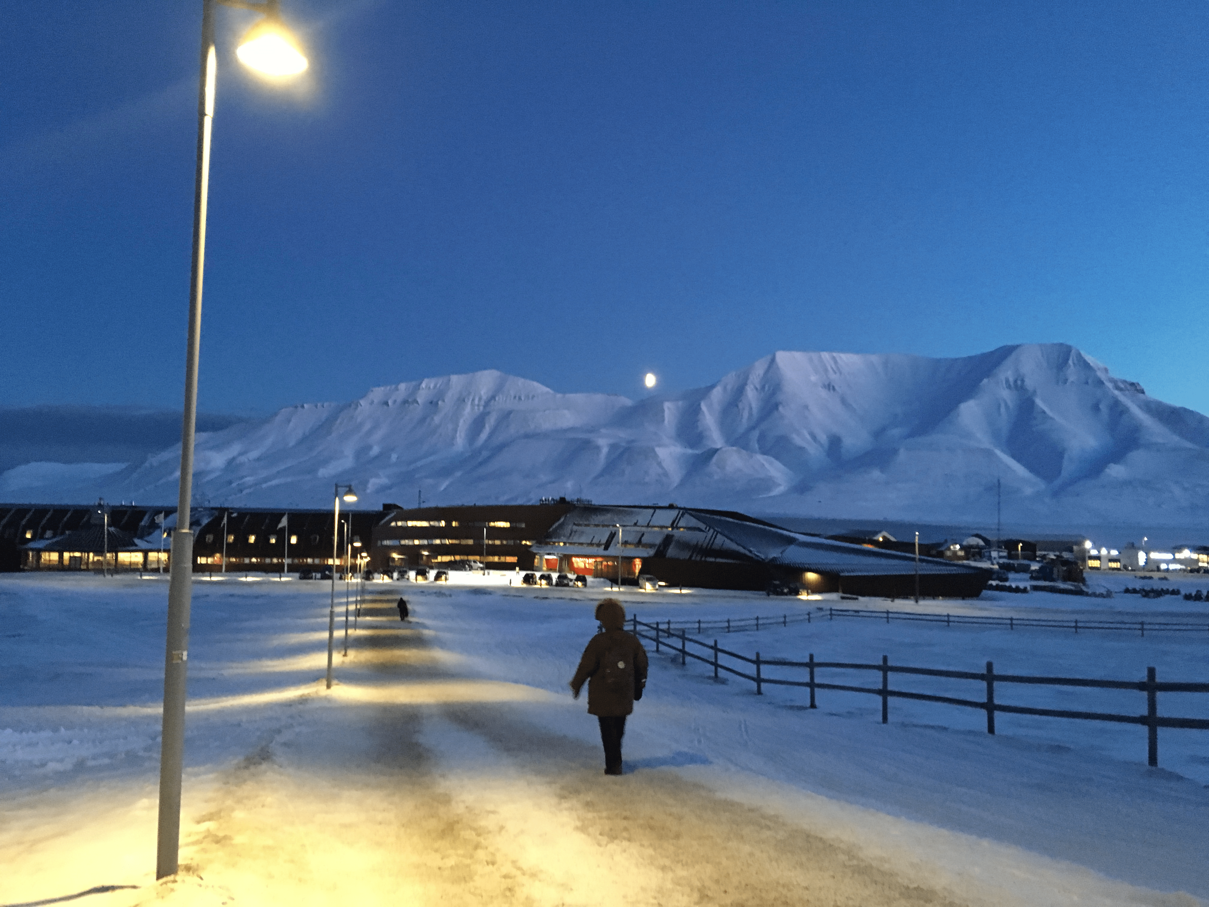 Student walking on dimly-lit path in snow with snowy mountains in background