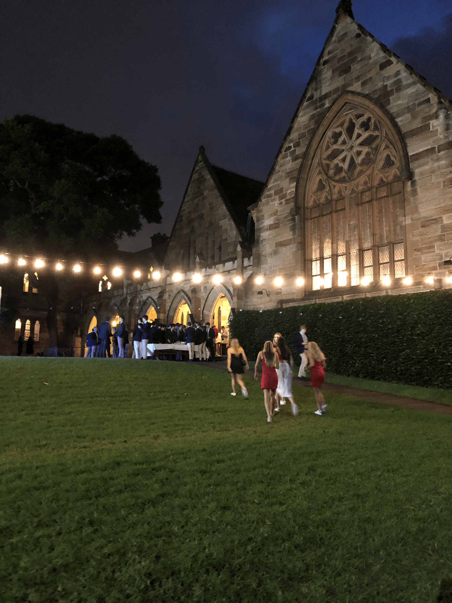 Old college building at night with string lights outside and students dressed up