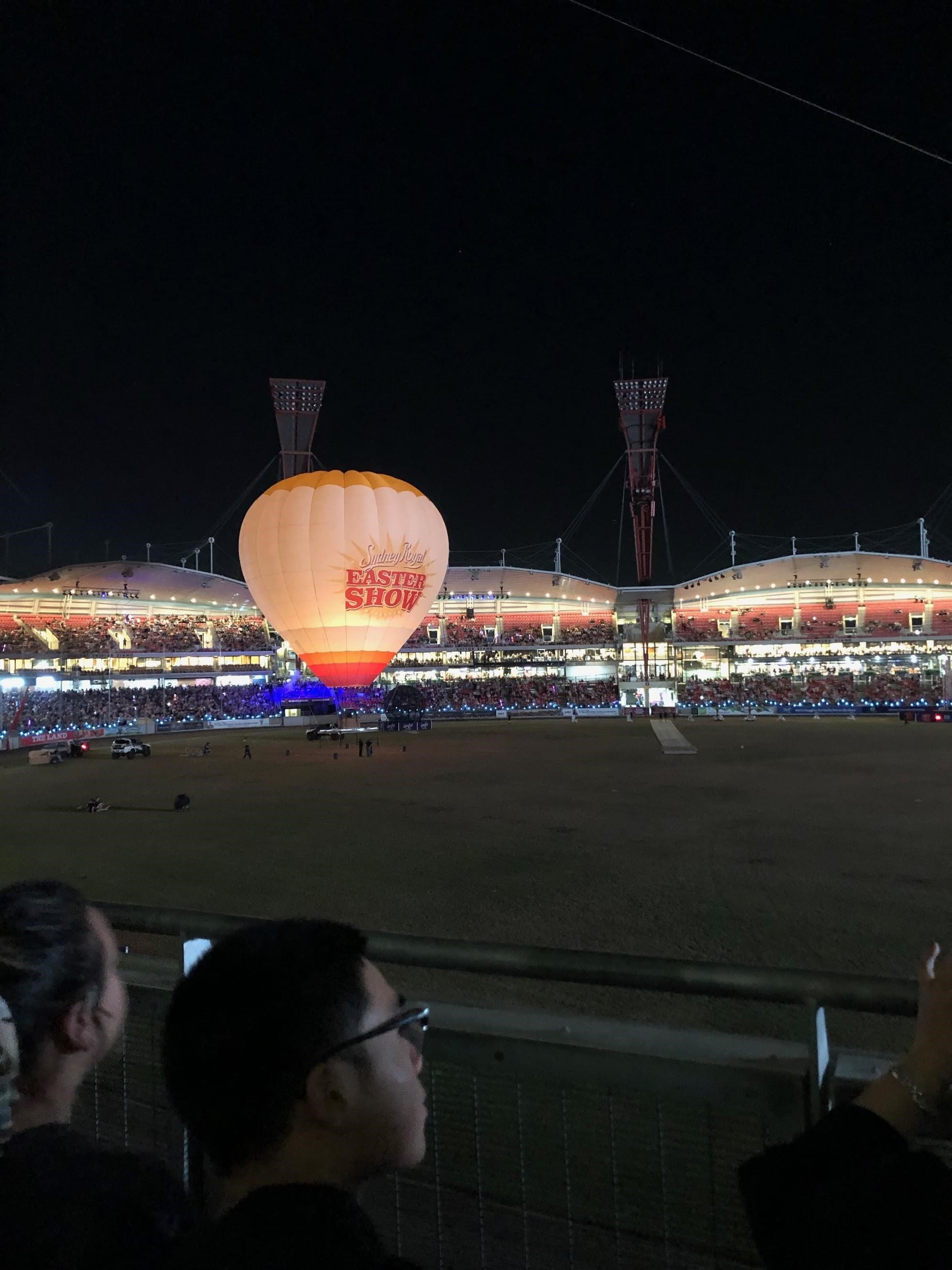 Hot air balloon on grass in stadium at night with bleachers and lights in background