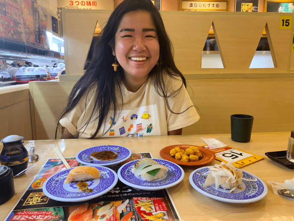 Cy smiles with plates of sushi on a table in front of her