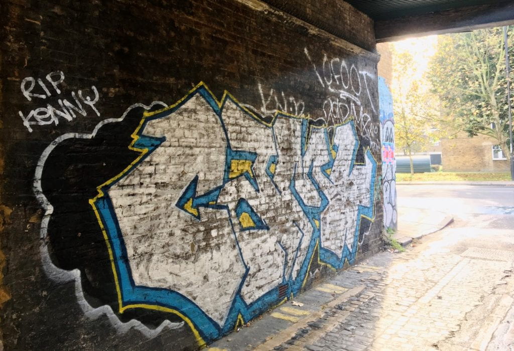 A graffiti covered wall under a bridge