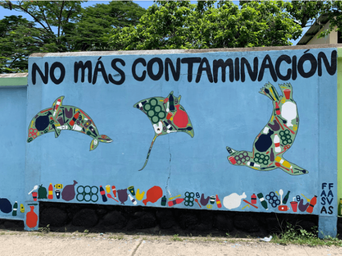 This mural depicts three iconic Galápagos marine species - a dolphin, a ray, and a sea lion - filled with plastic. The text at the top reads: “No more pollution.” There is a piece of litter in the lower right hand corner.