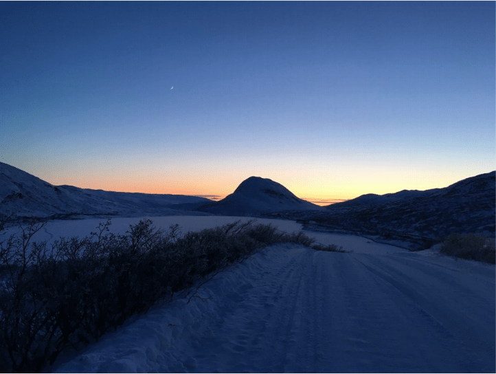 The sun sets behind a mountain with snow in the foreground